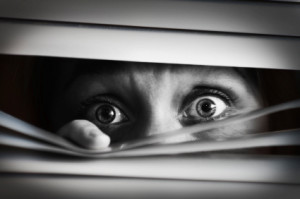 Scared woman peering through blinds