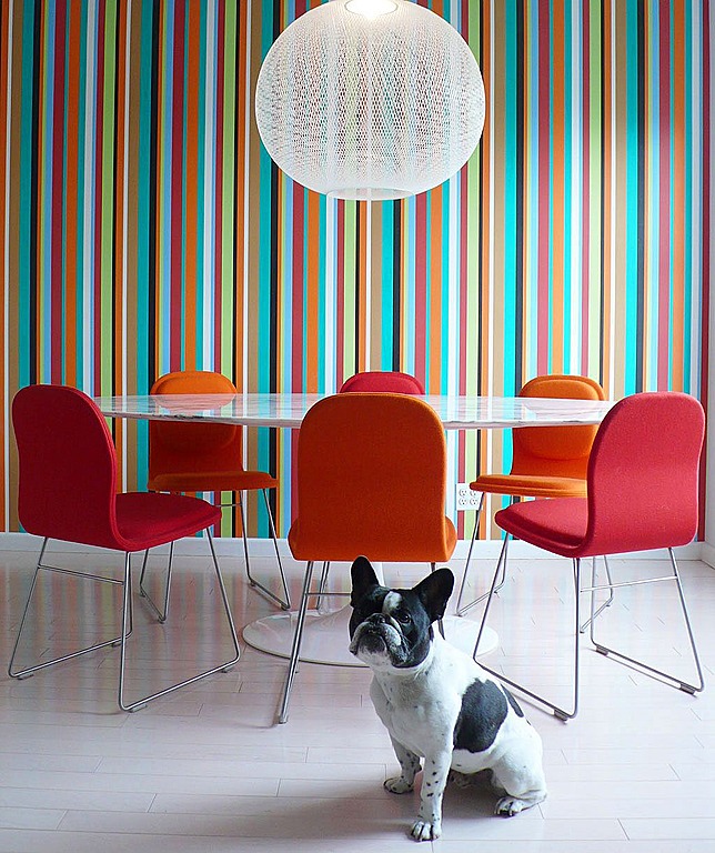 A white table and orange chairs balance the rainbow of colors in the wallpaper. By Alex Mundi Design